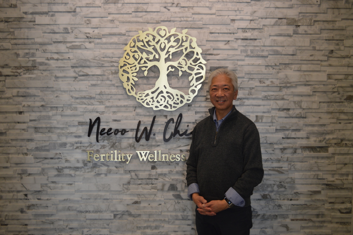 Dr. Chin smiling in front of logo